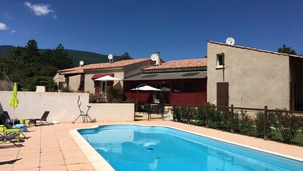 Una piscina con sillas de descanso y sombrillas, un edificio con antenas parabólicas, y montañas al fondo.