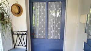 Una habitación con una puerta azul, una silla de metal, una mesita pequeña y una planta en maceta.