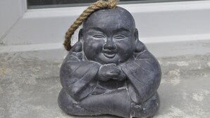 A stone Buddha statue with a rope on its head, placed on a concrete surface near a window.