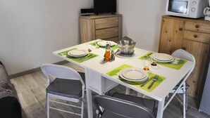 A dining area with a table set for four, including plates, cutlery, and a pitcher. There is a television on a wooden cabinet and a microwave on another cabinet.