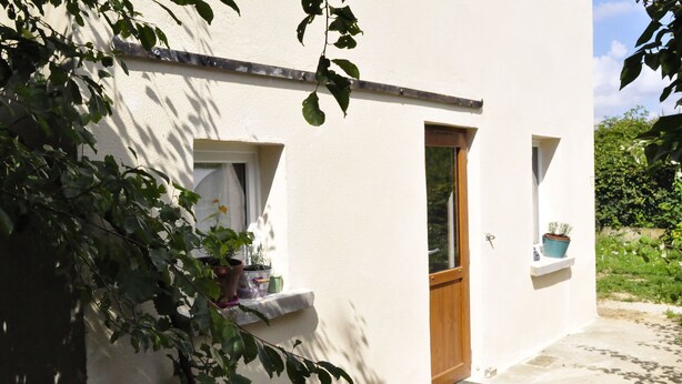 A white building with a wooden door and windows, surrounded by greenery.