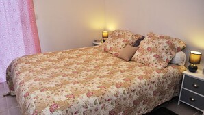 A neatly made bed with floral bedding, a bedside table with a lamp, and a window with a patterned curtain.
