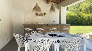 An outdoor dining area with a wooden ceiling, white chairs, and a table with a black and white tablecloth. - Pretty little independent house  (Dions)