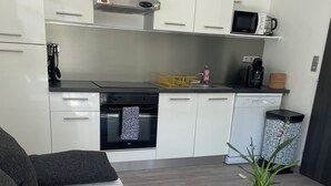 A modern kitchen with white cabinets, a microwave, a coffee maker, and a dishwasher. There is a small table with a plant and a sofa with dark cushions. - Pretty little independent house  (Dions)