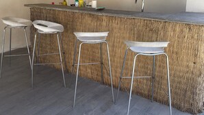 A kitchen with a bar area, two hanging light fixtures, a shelf with decorative items, and three bar stools. - Pretty little independent house  (Dions)