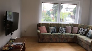 Una sala de estar con un sofá seccional, un televisor de pantalla plana montado en la pared y una mesa de centro de madera con aperitivos.