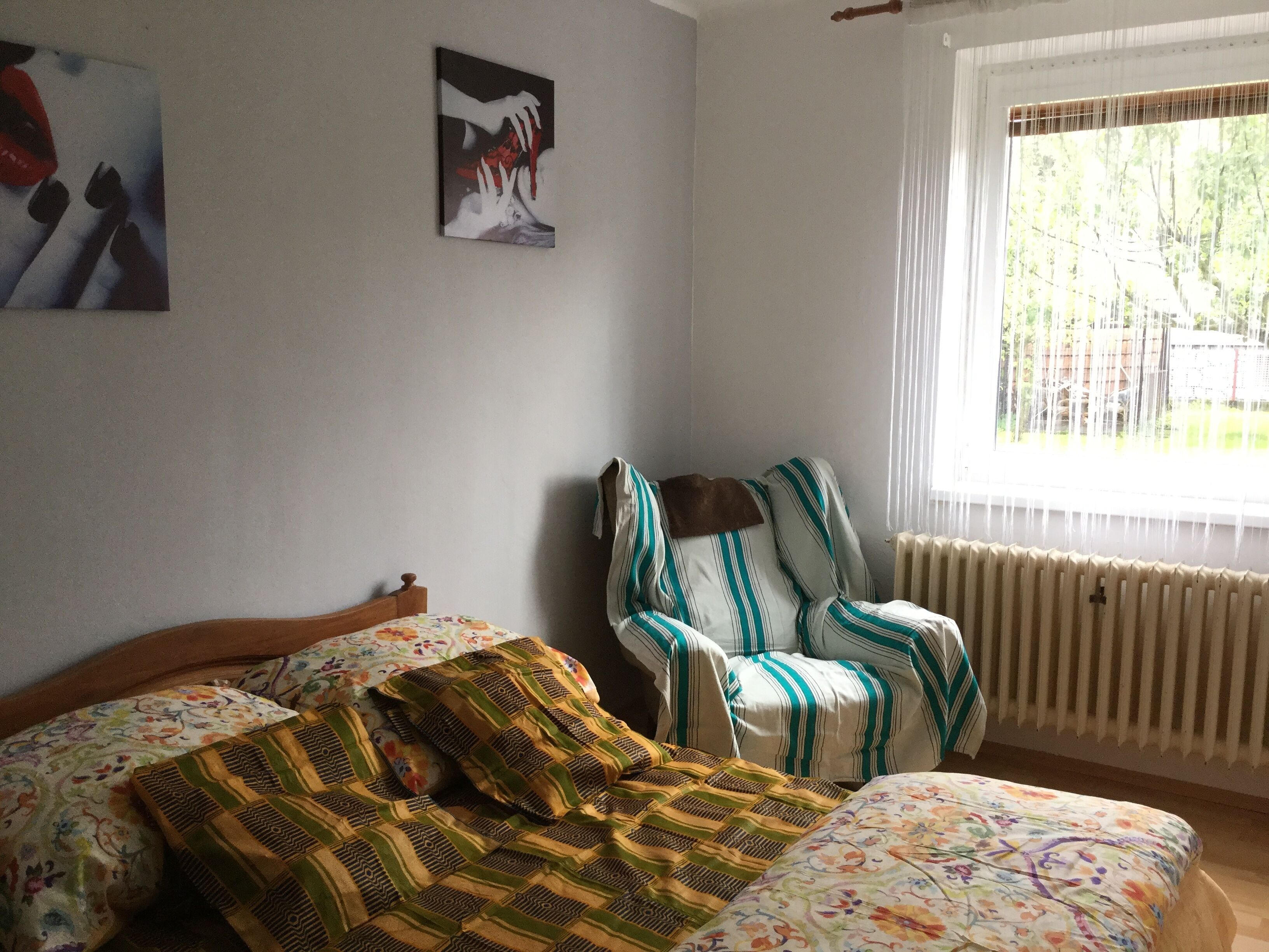 A bedroom with a bed, a chair, a radiator, and a window with a view of trees.