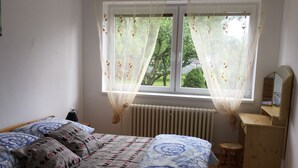 Un dormitorio con una cama, un aparador, un espejo y una ventana con cortinas translúcidas.