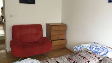 A room with a red armchair, a wooden chest of drawers, and a bed with patterned bedding.