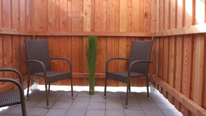 A wooden deck with two wicker chairs and a tall green plant in the center. - Modern apartment with terrace and use of sauna (Burgbernheim)