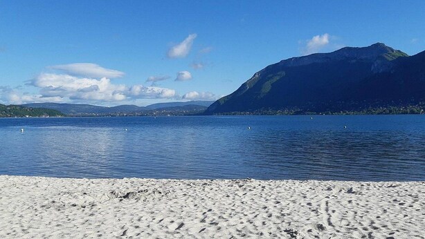 Een strand met een helder uitzicht op een meer en bergen op de achtergrond.
