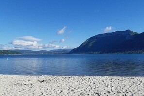 A beach with a clear view of a lake and mountains in the background.