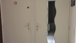 Een kamer met twee deuren, waarvan één een spiegel en een rookverbodsna bord heeft, en betegelde vloer.
