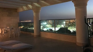 A rooftop terrace with lounge chairs, large windows, and a view of a cityscape at dusk. - Véronique luxuriou's penthouse (Eilat)