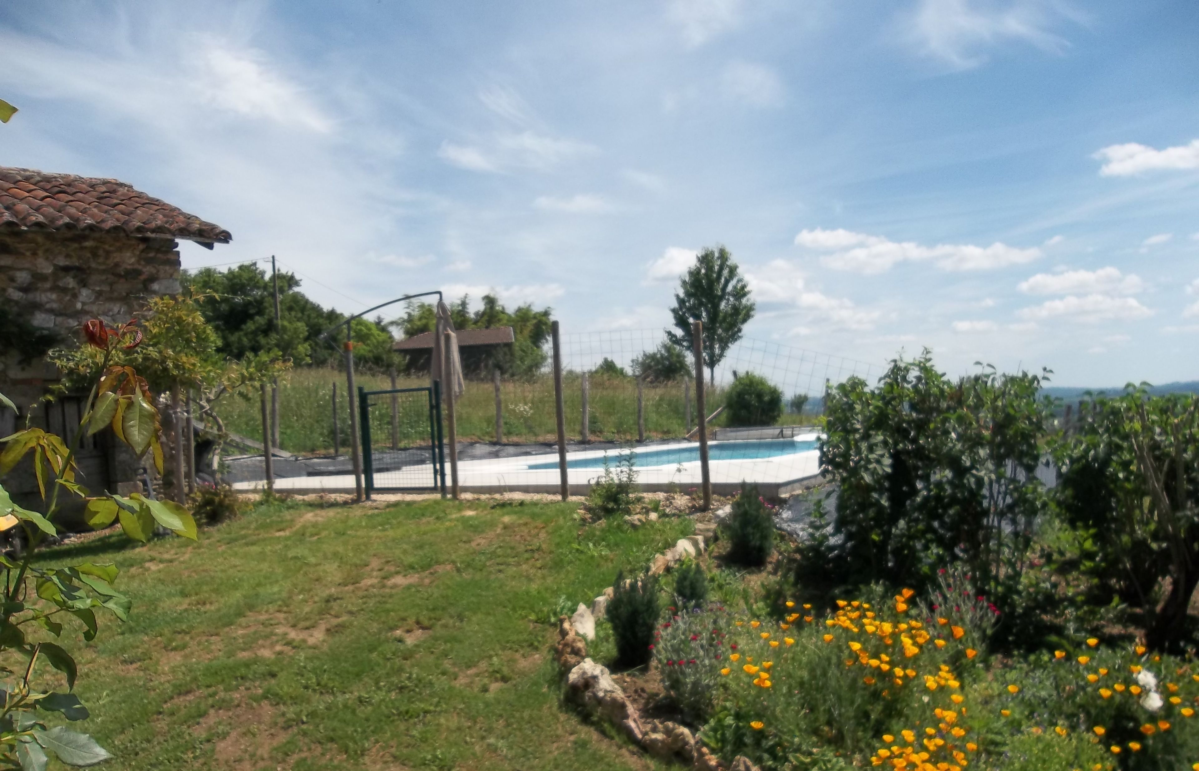 A backyard with a swimming pool, a stone house, and a garden with various plants and flowers.