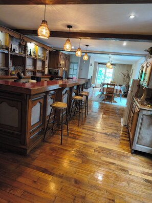 A spacious kitchen with wooden flooring, a bar area with stools, pendant lighting, and a view of the outdoors.