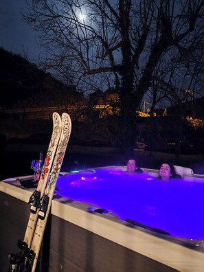 A hot tub with skis leaning against it, surrounded by trees and a night sky.