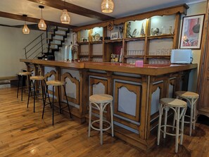 Een bar met houten barstoelen, een toonbank met glazen en een trap.