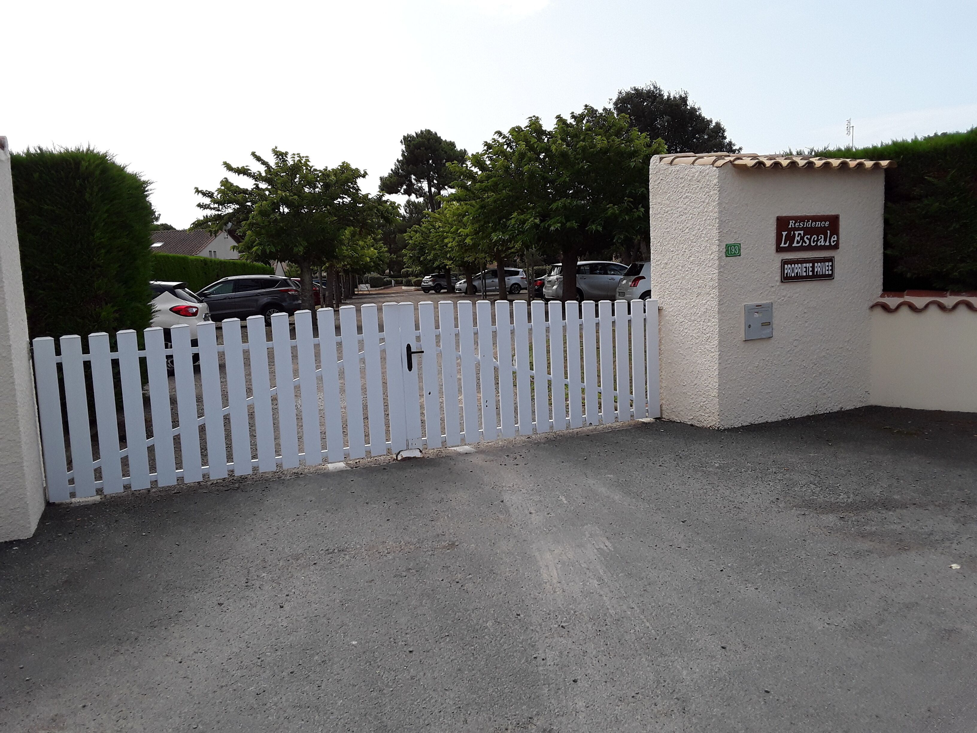A gated entrance with a white picket fence, a sign reading "Residence L'Escale," and a number "193" indicating the property.
