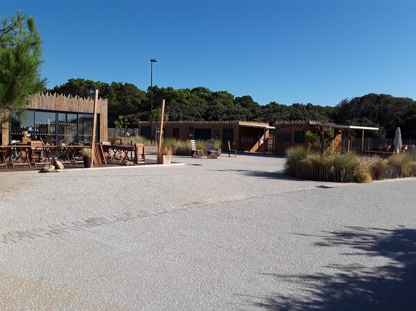 A spacious outdoor area with a gravel ground, wooden furniture, and a building with large windows and a wooden fence.