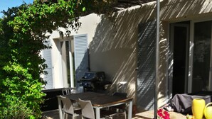 En udendørs patio med et bord, stole, grill og krukkeplanter.