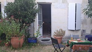 Eine kleine Terrasse im Freien mit einem Tisch für zwei Personen, umgeben von Topfpflanzen und einem Schachbrettboden.