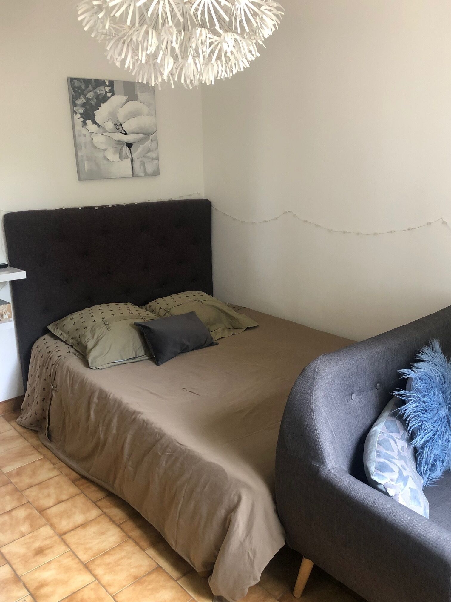 Un dormitorio con cama, mesita de noche, una silla y lámpara colgante.