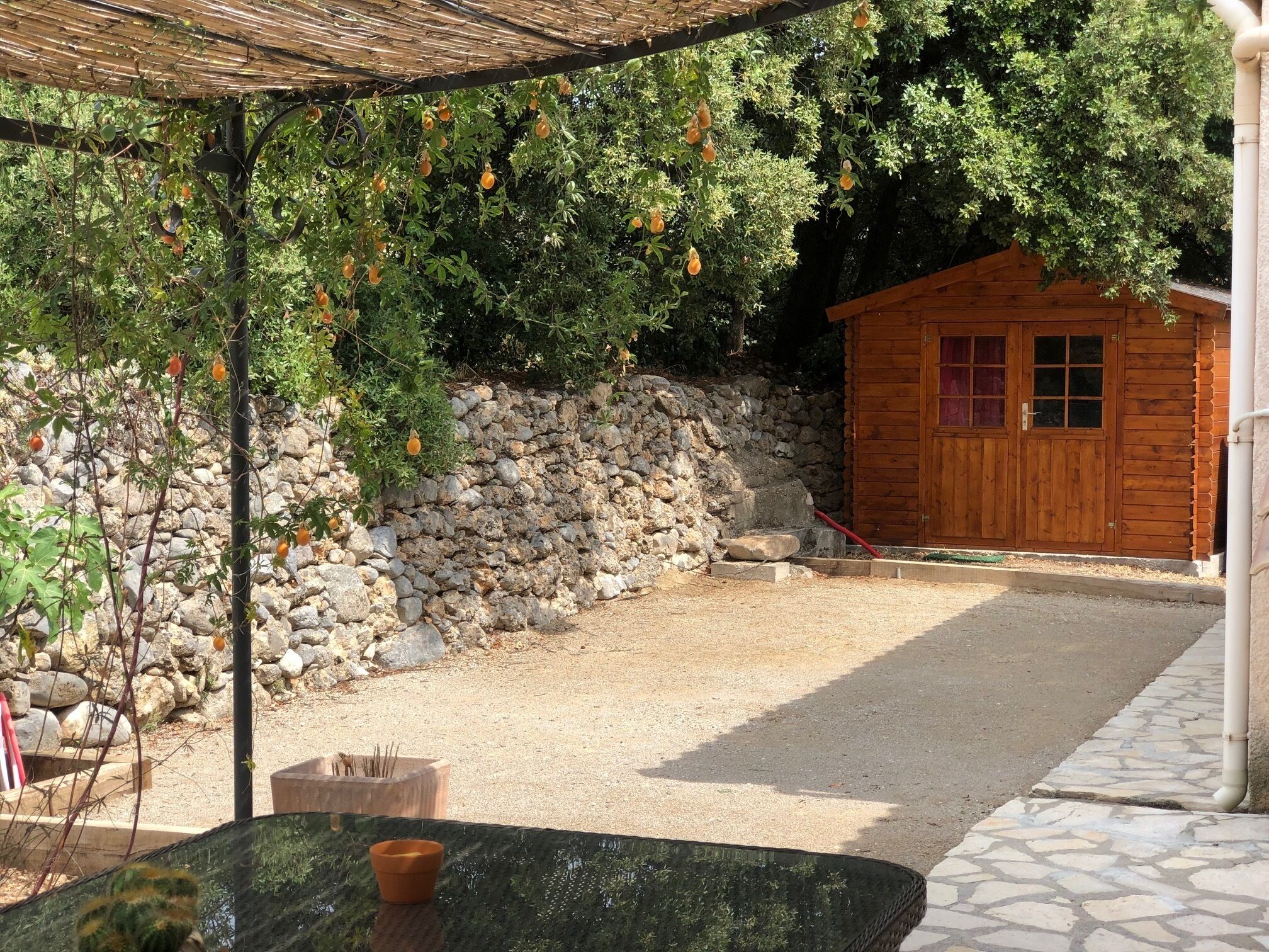 Un espacio al aire libre cubierto con un muro de piedra, un cobertizo de madera y un camino de grava.