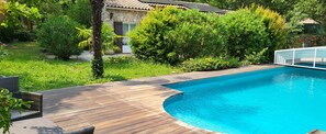 A swimming pool with a wooden deck, surrounded by lush greenery and a stone building. - Exceptional setting for a villa with 4,800 m² of land (Fayence)