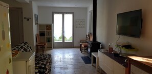 A compact living space with a kitchenette, a sofa, a television, and a sliding glass door leading to a balcony.