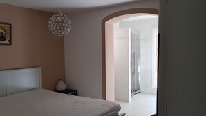 A bedroom with a bed, a nightstand, a decorative lamp, a framed picture on the wall, and a shower area visible through an archway. - Exceptional setting for a villa with 4,800 m² of land (Fayence)