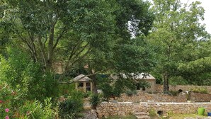 A stone wall with a small wooden structure, surrounded by lush greenery and flowering plants. - Exceptional setting for a villa with 4,800 m² of land (Fayence)
