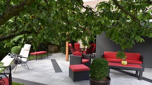 An outdoor patio with wicker furniture, red cushions, and a potted plant.