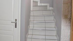 A staircase with white steps leading to a landing, a white door to the left, and a stone wall on the right.