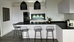 A modern kitchen with white cabinetry, a central island with bar stools, a built-in oven, and pendant lighting. - BEAUTIFUL APARTMENT WITH SEA VIEW TERRACE- NEAR BEACH - IDEAL FAMILY HOLIDAYS (Roses)