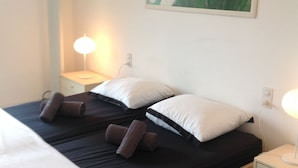 A double bed with black and white bedding, two pillows, and two rolled towels. There is a bedside table with a lamp and a painting of flowers on the wall. - BEAUTIFUL APARTMENT WITH SEA VIEW TERRACE- NEAR BEACH - IDEAL FAMILY HOLIDAYS (Roses)