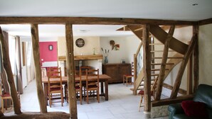 A rustic interior with exposed wooden beams, a dining area with wooden chairs and a table, a staircase, and a green leather sofa. - House completely renovated in the countryside in tourist village (Saint-Evroult-Notre-Dame-du-Bois)