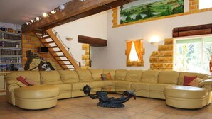 A living room with a beige sectional sofa, a glass coffee table, a staircase, a bookshelf, and a painting on the wall. - Comfortable farmhouse with private pool and festive bar for 14 people (Sérignan-Du-Comtat)