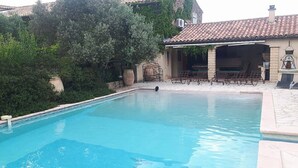 A swimming pool with a tiled deck, surrounded by greenery and a building with a tiled roof. - Comfortable farmhouse with private pool and festive bar for 14 people (Sérignan-Du-Comtat)