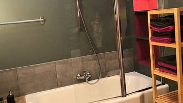 A modern bathroom with a bathtub, a glass shower enclosure, and a wooden shelf with towels.