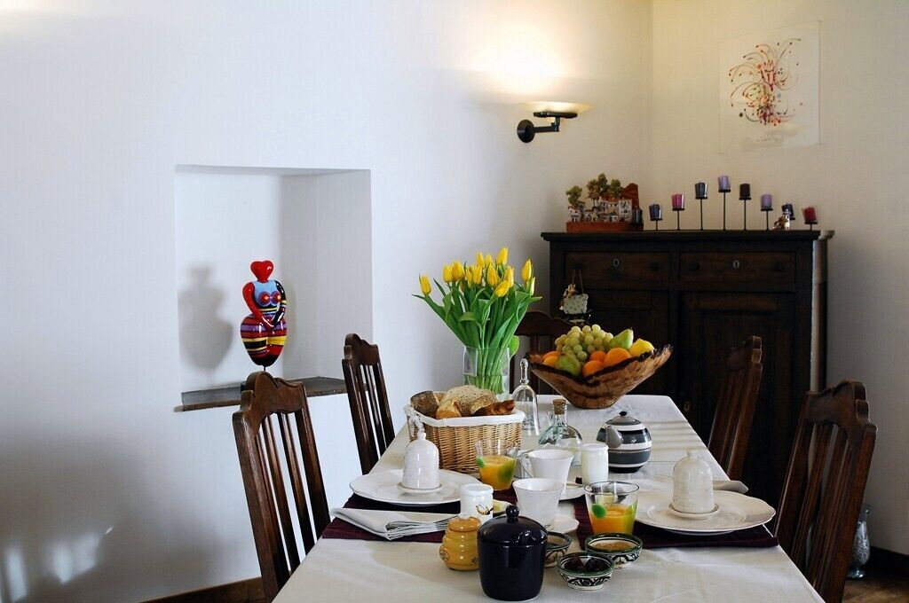 Ein Esstisch, gedeckt mit Frühstücksleckereien, eine Vase mit gelben Tulpen und ein Obstkorb.