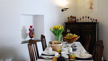 Ein Esstisch, gedeckt mit Frühstücksleckereien, eine Vase mit gelben Tulpen und ein Obstkorb.