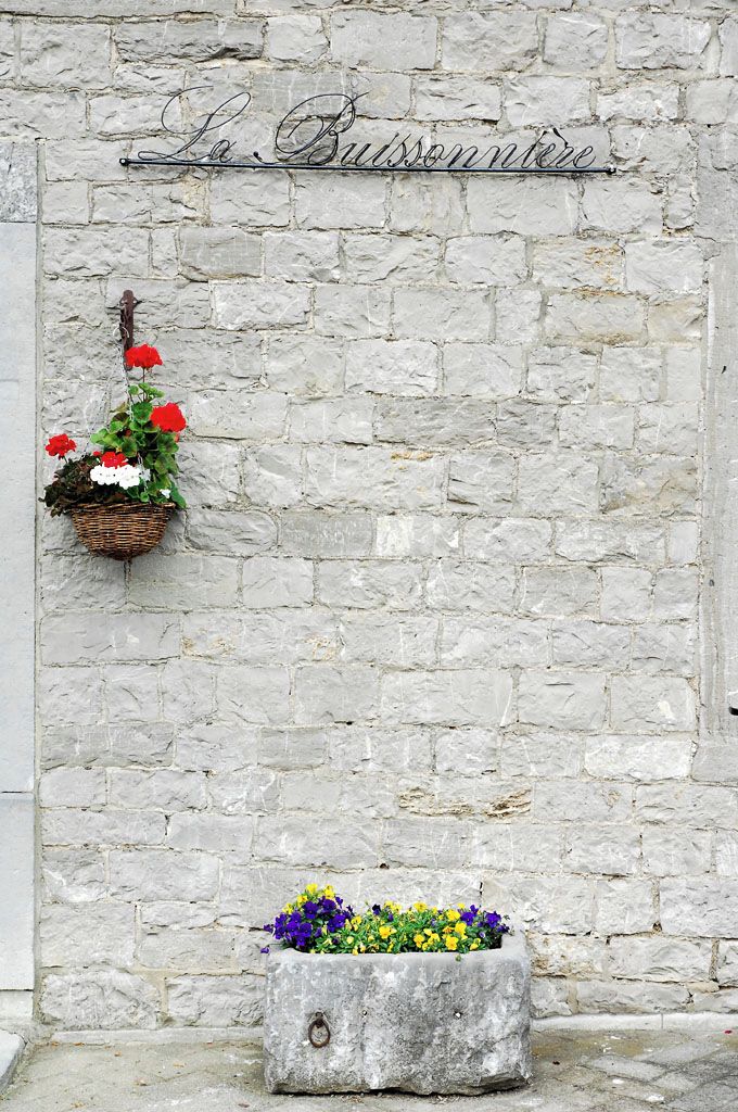 Eine Steinsäule mit einem hängenden Korb voller roter und weißer Blumen und einem Steintopf mit violetten und gelben Blüten.