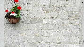 Eine Steinsäule mit einem hängenden Korb voller roter und weißer Blumen und einem Steintopf mit violetten und gelben Blüten.