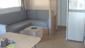 Eine kompakte Küchenzeile mit Mikrowelle und Kühlschrank, ein graues Sofa mit kleinem Tisch und ein Fenster mit Vorhängen.