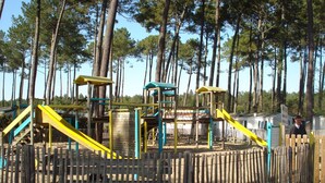 Ein Spielplatz mit Holzzaun, gelb-blauen Spielgeräten und blauem Himmel.
