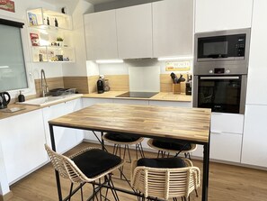 A modern kitchen with white cabinets, a wooden table, wicker chairs, a built-in microwave, and an oven.