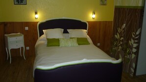 Una cama con cabecera oscura, dos lámparas de noche, una mesita de noche y un almohadón verde.