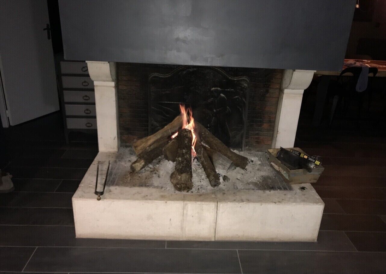 Une cheminée avec un feu qui crépite, entourée d’un manteau de cheminée blanc et surplombant un sol carrelé.