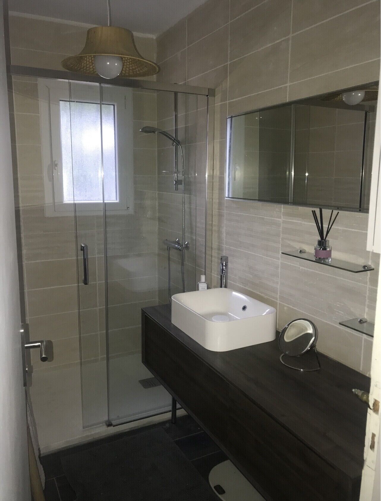 Een moderne badkamer met een douchecabine van glas, een witte wastafel en een donker aanrecht.